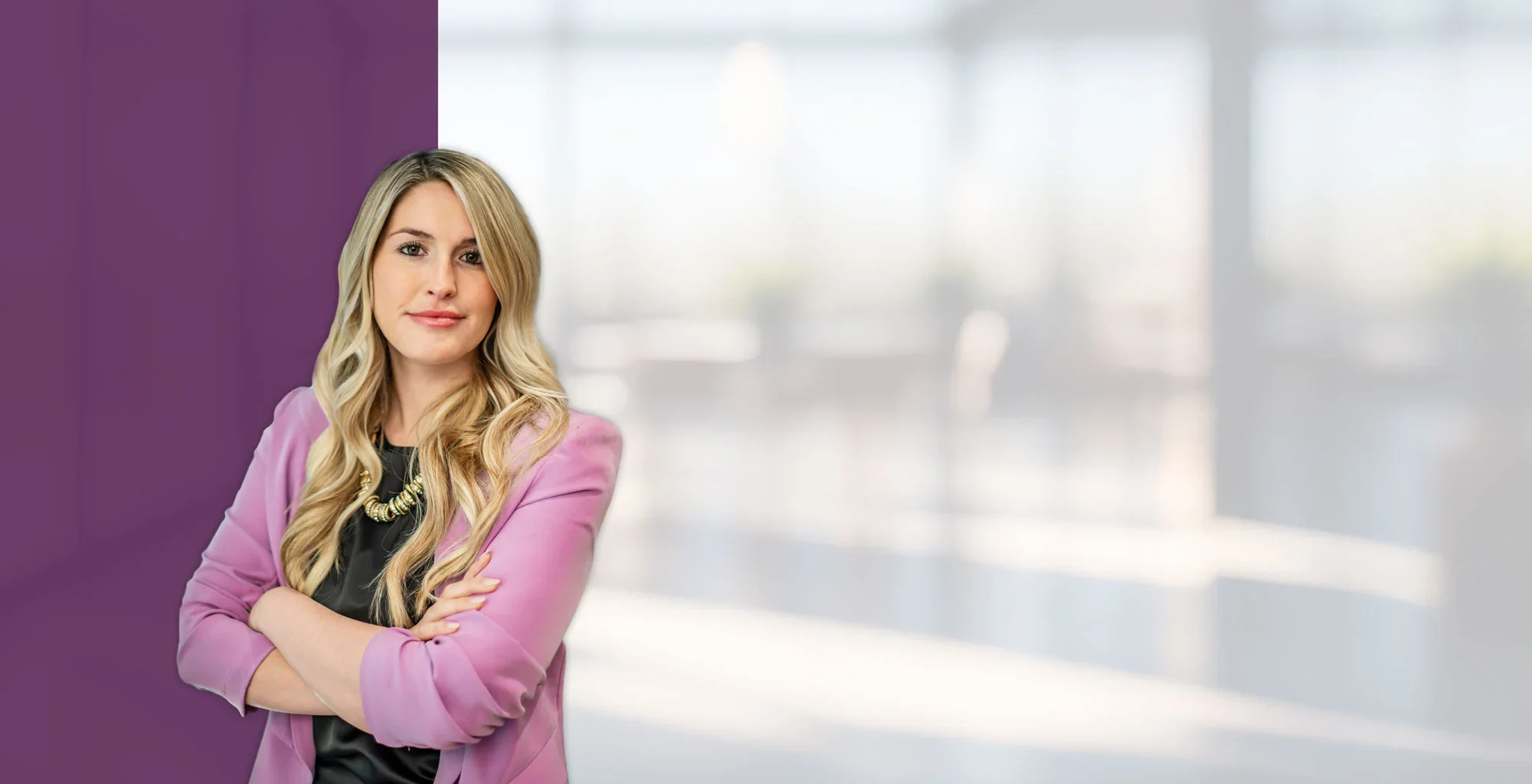 Alexandria Crouthamel standing confidently with arms crossed, wearing a pink blazer and black top, in a bright modern office with a purple accent wall